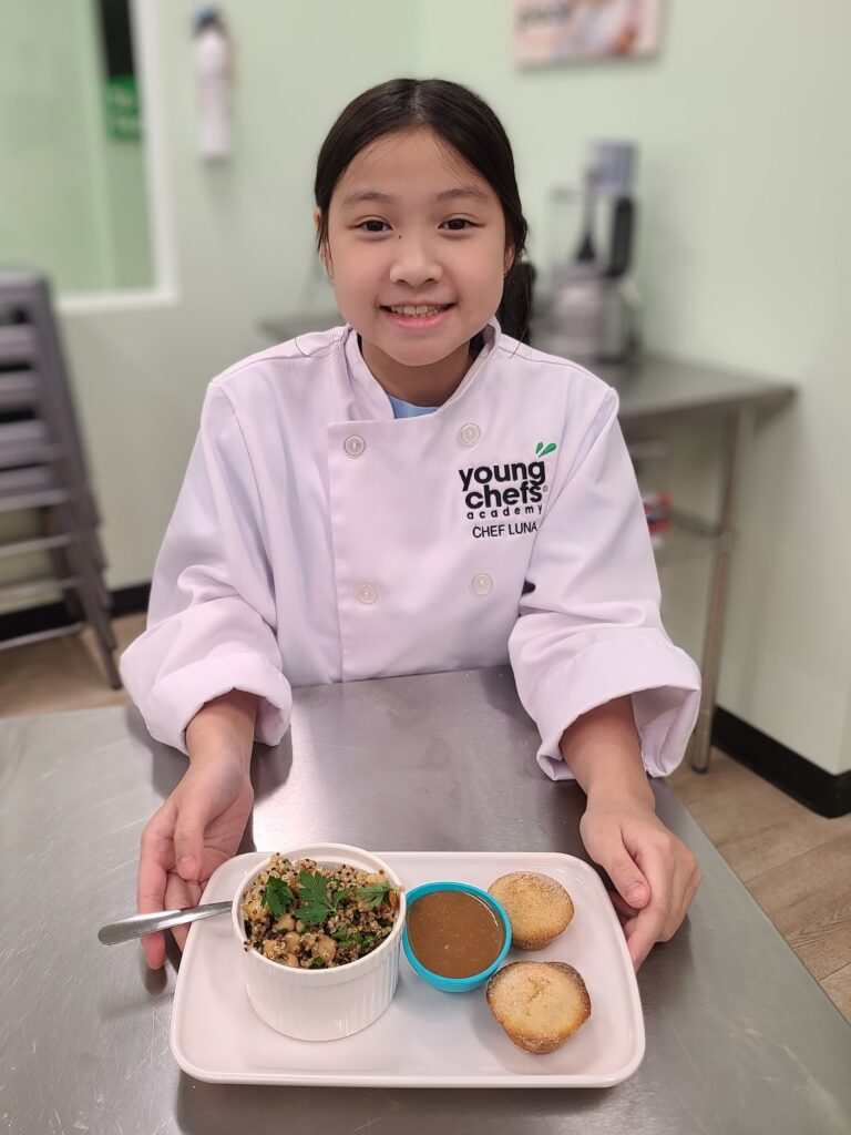 Young Chefs Academy student proudly presenting her completed meal in a real kitchen cooking class in Austin