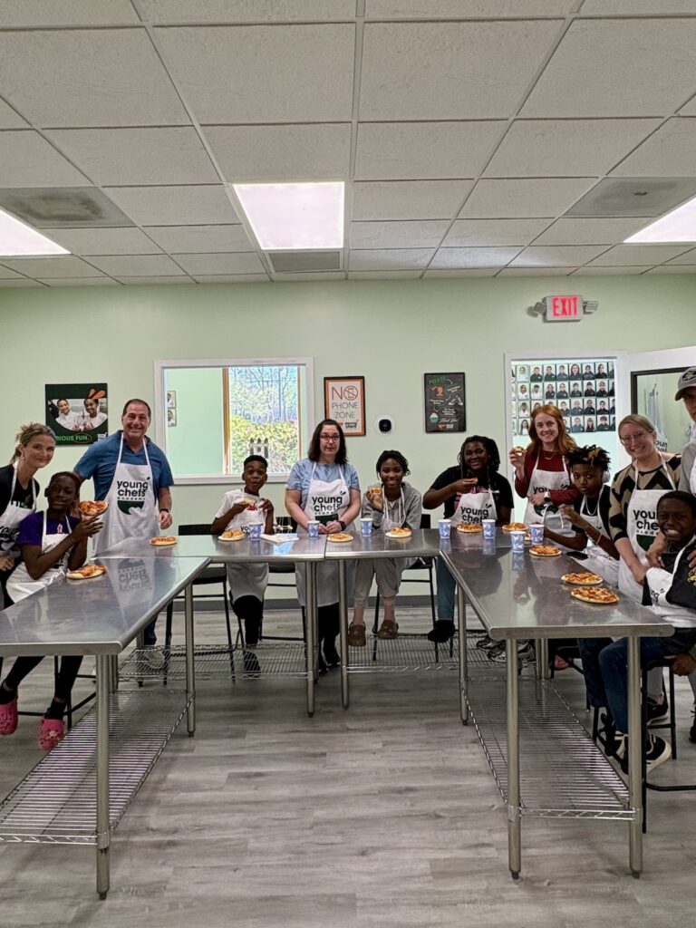 Group of students and instructors enjoying pizza together during a Young Chefs Academy cooking class in a professional teaching kitchen