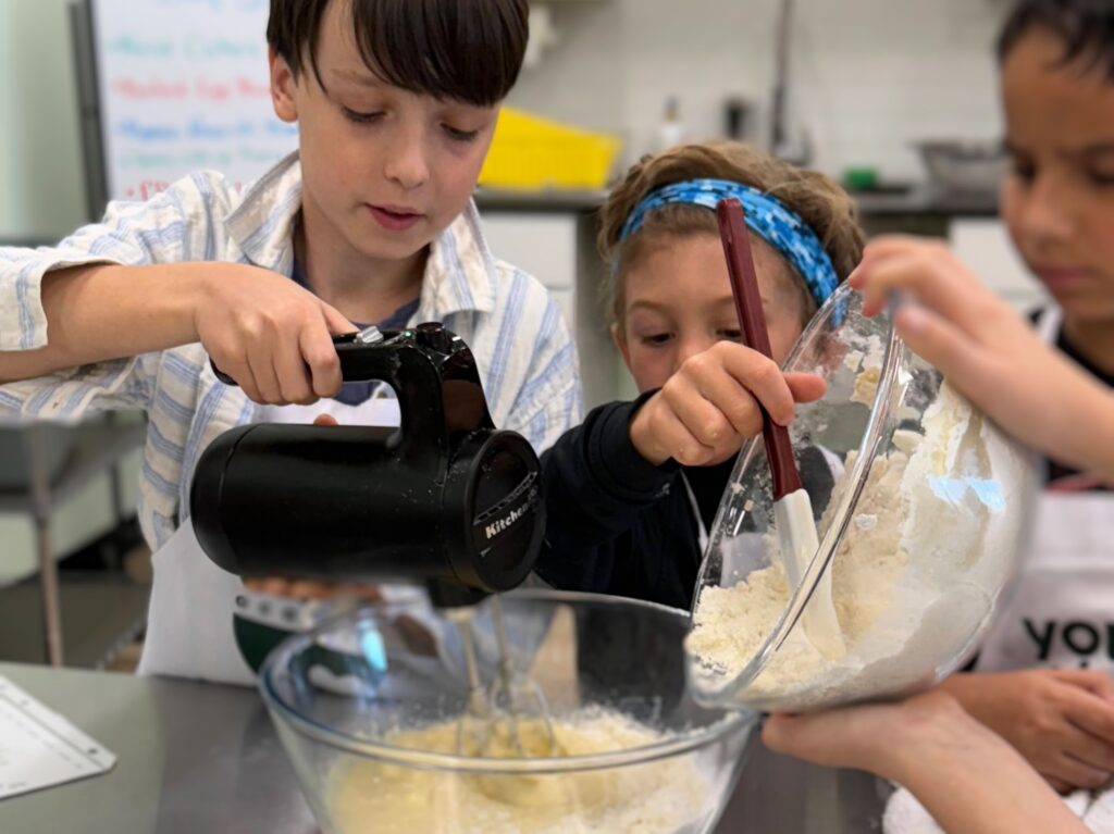 Kids working together with real kitchen equipment during a cooking class at Young Chefs Academy Austin