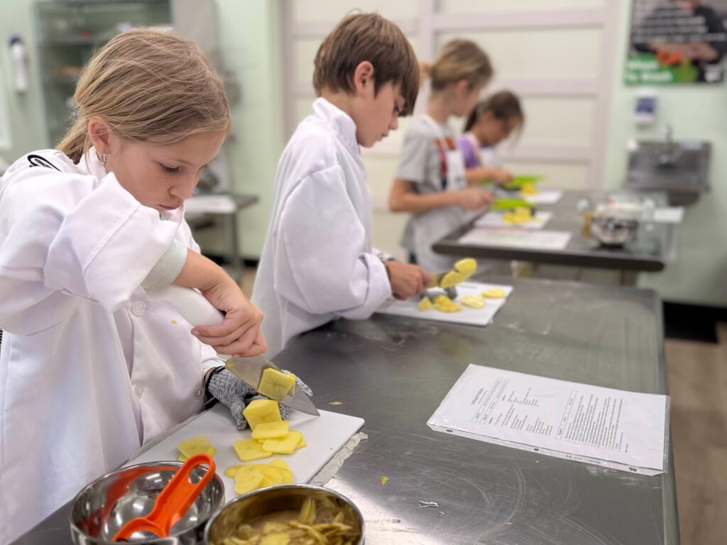 Children practicing safe knife skills with cut-resistant gloves in a real kitchen cooking class in Austin