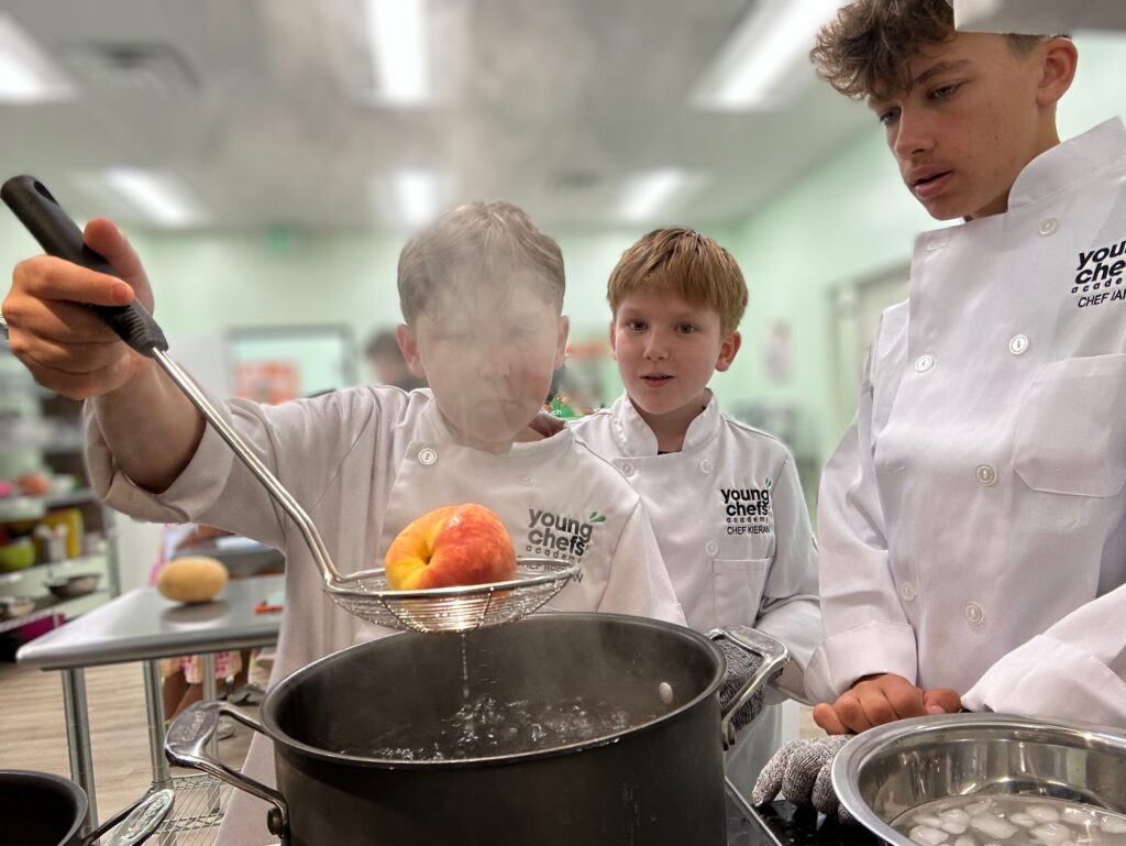 Young chefs learning to blanch fruit on a real stovetop at Young Chefs Academy Austin cooking class