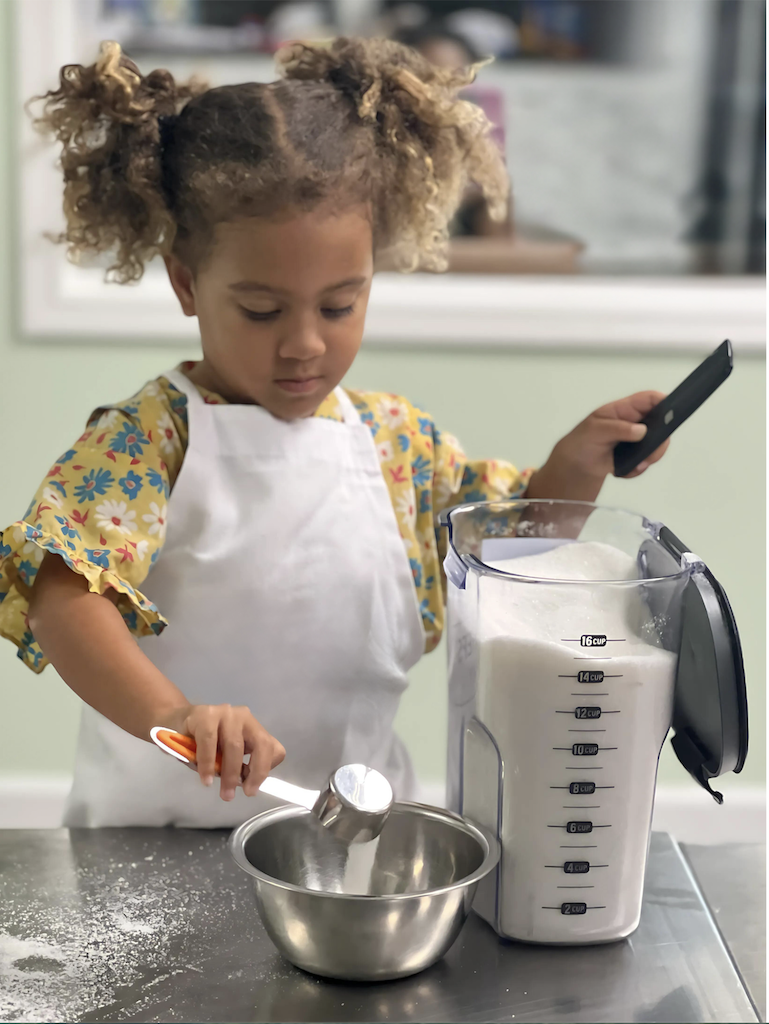 Young girl in a white apron measuring flour into a bowl during a Young Chefs Academy cooking class